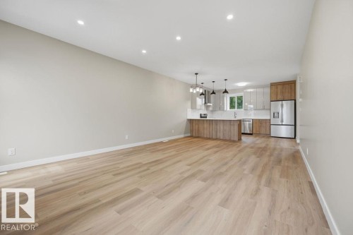 Open-concept living space featuring wood-finish flooring, recessed ceiling lighting, and a contemporary kitchen - 15004 62 Street, Edmonton, AB 