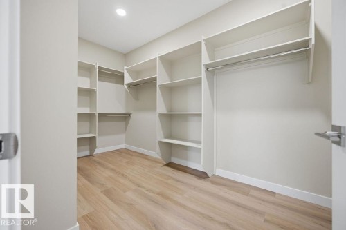 Walk-in closet featuring extensive built-in shelving, multiple hanging rods, recessed ceiling lighting, and wood-finish flooring - 15004 62 Street, Edmonton, AB 