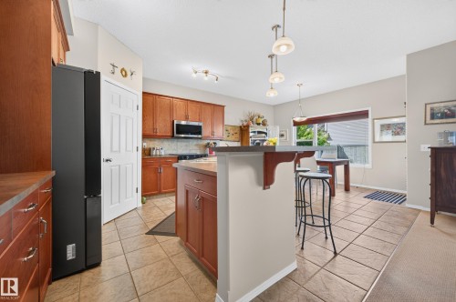 Kitchen featuring a central island with an extended countertop, wood cabinetry, tile flooring, and a stainless steel microwave - 1310 82 Street, Edmonton, AB 