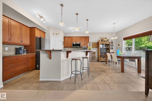 Open-concept kitchen and dining area featuring wood cabinetry, integrated appliances, a breakfast bar, recessed lighting, and large format floor tiling - 1310 82 Street, Edmonton, AB 