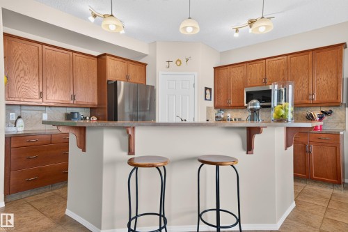 Kitchen featuring a breakfast bar with corbel accents, stainless steel appliances, wood cabinetry, tile flooring, and a tile backsplash - 1310 82 Street, Edmonton, AB 
