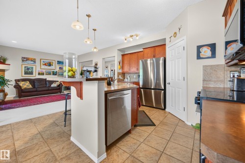 Kitchen featuring tile flooring, stainless steel appliances, wood cabinetry, and a peninsula with a breakfast bar - 1310 82 Street, Edmonton, AB 