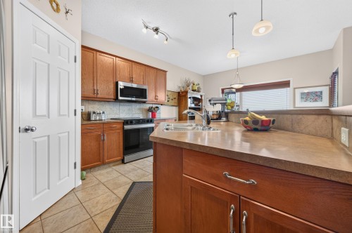 Kitchen featuring warm wood cabinetry, stainless steel appliances, a tile backsplash, and a breakfast bar with pendant lighting - 1310 82 Street, Edmonton, AB 