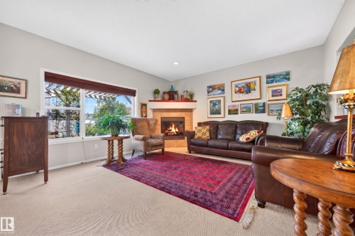Living area featuring a tile-surround fireplace with a wood mantel, expansive window with exterior pergola, recessed lighting, and neutral carpeting - 1310 82 Street, Edmonton, AB 