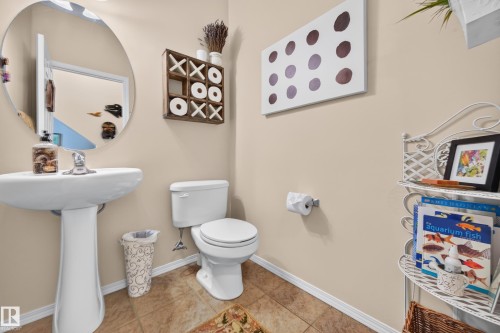 Pedestal sink with a round mirror, complemented by a white toilet and tile flooring - 1310 82 Street, Edmonton, AB 