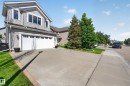 Two-story home featuring light gray horizontal siding, an attached two-car garage with paneling and window inserts, a concrete driveway, and a manicured lawn with mature trees - 1310 82 Street, Edmonton, AB 