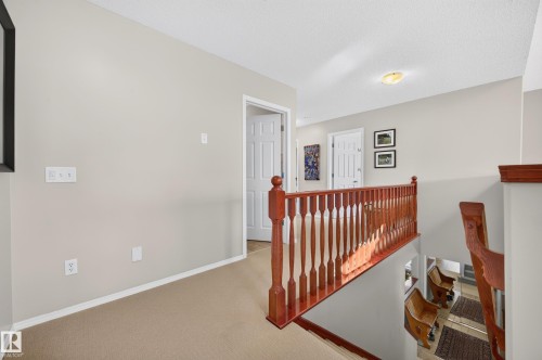 Hallway featuring light-colored walls, carpeted flooring, and a wood-finish banister - 1310 82 Street, Edmonton, AB 