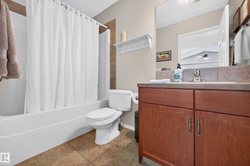 Bathroom featuring a white bathtub, ceramic tile flooring, a built-in wood-finish vanity with a countertop, and a toilet - 1310 82 Street, Edmonton, AB 