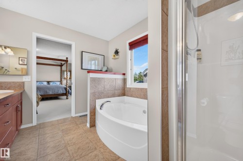 Bathroom featuring a corner soaking tub with tile surround, a separate shower enclosure, a single vanity with stone-finish countertop, and tile flooring - 1310 82 Street, Edmonton, AB 