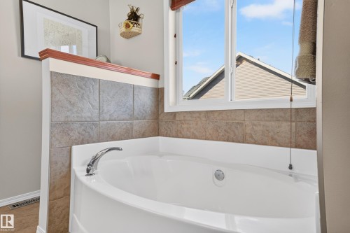 Soaking tub with chrome fixtures, surrounded by textured tile and a decorative wood ledge - 1310 82 Street, Edmonton, AB 