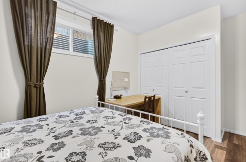Room featuring a window with a built-in blind, white bi-fold closet doors, and wood-finish flooring - 1310 82 Street, Edmonton, AB 