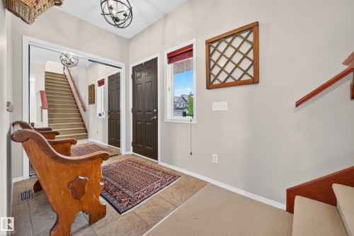 Foyer entry with tile flooring, a dark paneled door, and a staircase with carpeted treads and a wood handrail - 1310 82 Street, Edmonton, AB 