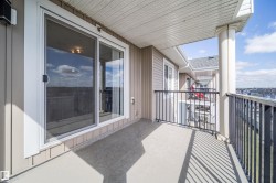 Private balcony with concrete flooring and black metal railings, featuring a sliding glass door entry, exterior siding, and a white soffit ceiling - 