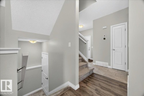 Split-level entry featuring wood-finish flooring, neutral wall paint, and a carpeted staircase - 17203 71 Street, Edmonton, AB 