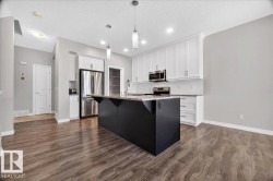 Modern kitchen featuring a large black island with a stone-finish countertop, white upper and lower cabinetry, stainless steel appliances, and wood-finish flooring - 