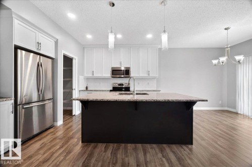 Kitchen featuring a central island with a granite countertop, stainless steel appliances, recessed lighting, wood-finish flooring, and white cabinetry - 17203 71 Street, Edmonton, AB 