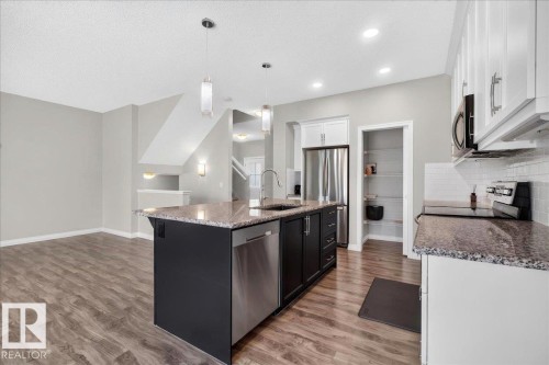 Modern kitchen featuring an island with a stainless steel dishwasher, a stainless steel refrigerator, white cabinetry, a subway tile backsplash, and wood-finish flooring - 17203 71 Street, Edmonton, AB 