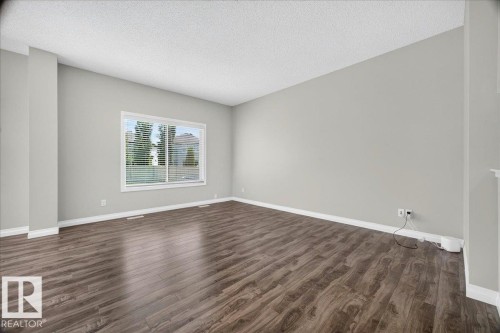 Expansive room featuring wood-finish flooring, light grey painted walls, white baseboards, and a large window with white blinds - 17203 71 Street, Edmonton, AB 