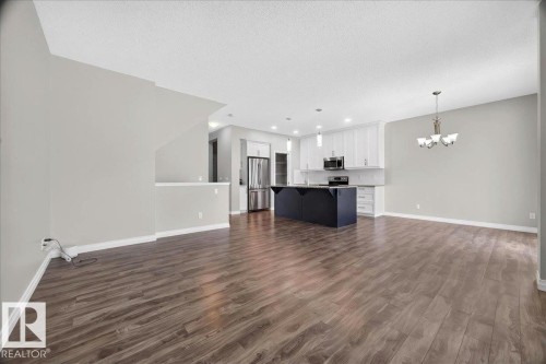 Open-concept living space featuring wood-finish flooring, a contemporary kitchen with a dark island, stainless steel appliances, and white cabinetry - 17203 71 Street, Edmonton, AB 