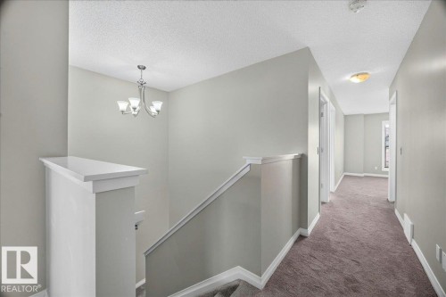 Upper-level hallway featuring a neutral color palette, plush carpeting, white trim, recessed lighting, and a contemporary chandelier - 17203 71 Street, Edmonton, AB 
