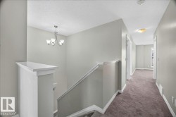Upper-level hallway featuring a neutral color palette, plush carpeting, white trim, recessed lighting, and a contemporary chandelier - 