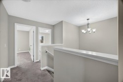 Upper-level hallway featuring a chandelier, light gray wall paint, and gray carpeting - 