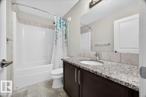 Bathroom featuring a dark wood-finish vanity with a speckled countertop, an undermount sink, and a large wall-mounted mirror - 17203 71 Street, Edmonton, AB 