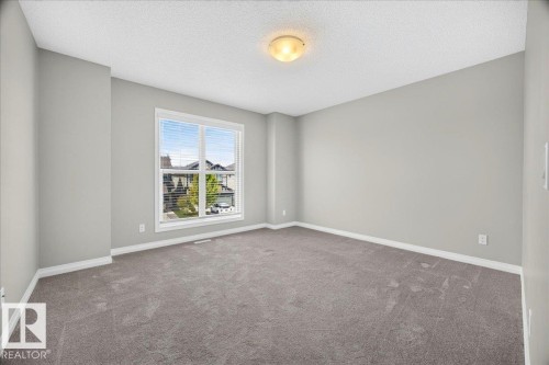 Spacious room featuring a large window with horizontal blinds, neutral-toned walls, gray carpeting, and white baseboards - 17203 71 Street, Edmonton, AB 