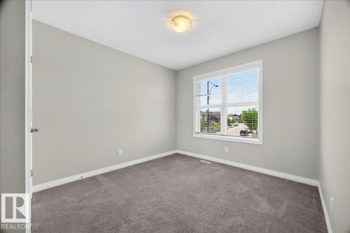 Bright room featuring a large window with white blinds, neutral gray walls, and gray carpeting - 17203 71 Street, Edmonton, AB 