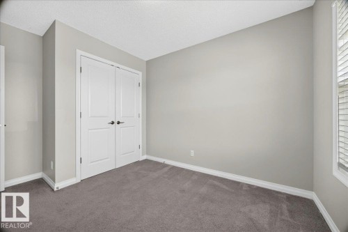 Spacious room featuring neutral painted walls, gray carpet flooring, white baseboards, and a double-door closet with dark hardware - 17203 71 Street, Edmonton, AB 