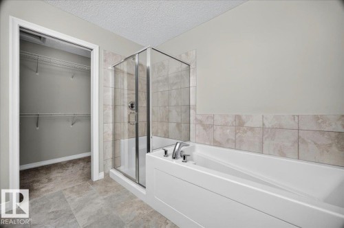 Modern bathroom featuring a glass-enclosed shower, a white soaking tub with chrome fixtures, and a tiled accent wall - 17203 71 Street, Edmonton, AB 