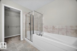 Modern bathroom featuring a glass-enclosed shower, a white soaking tub with chrome fixtures, and a tiled accent wall - 