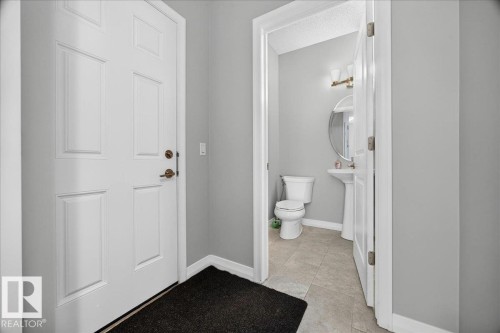 Entryway with paneled white door and bronze hardware, featuring a powder room with a pedestal sink, round mirror, and tile flooring - 17203 71 Street, Edmonton, AB 