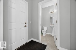 Entryway with paneled white door and bronze hardware, featuring a powder room with a pedestal sink, round mirror, and tile flooring - 