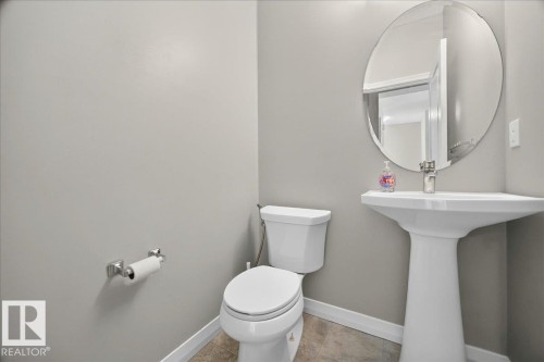 Bathroom featuring a white pedestal sink with a chrome faucet, a coordinating white toilet, and a circular wall-mounted mirror - 17203 71 Street, Edmonton, AB 