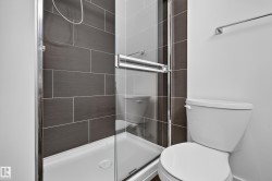 Walk-in shower featuring a sliding glass door, dark rectangular wall tiles, and a white shower pan - 