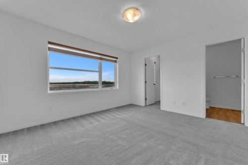Spacious room featuring light gray carpeting, a large window with roller shades, and two interior doorways - 144 Sunwapta Way, Edmonton, AB 