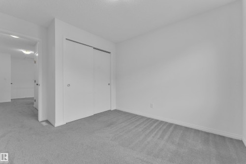 Room featuring light grey carpeting, white walls, white trim, and a built-in closet with white sliding doors - 144 Sunwapta Way, Edmonton, AB 