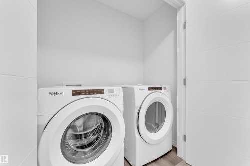 Dedicated laundry area featuring a front-loading washer and dryer, wood-finish flooring, and a modern white door with horizontal paneling - 144 Sunwapta Way, Edmonton, AB 