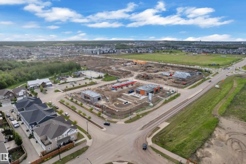 Expansive aerial capture showcasing a developing neighborhood with established residential properties, new commercial construction, and undeveloped green spaces - 144 Sunwapta Way, Edmonton, AB 