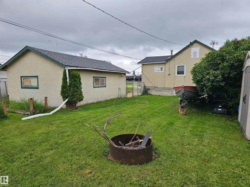 Expansive grassy yard with a fire pit, mature landscaping, and privacy fencing - 5305 46 Street, Leduc, AB 