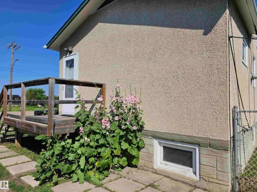 Stucco exterior featuring a wooden deck with railing, a white entry door, a basement window, and a chain-link fence - 5305 46 Street, Leduc, AB - Outdoor With Exterior