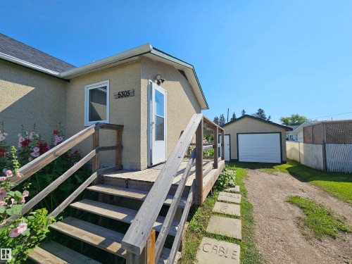 Exterior featuring stucco siding, a wood-plank deck, and a detached single-car garage with a white overhead door - 5305 46 Street, Leduc, AB - Outdoor