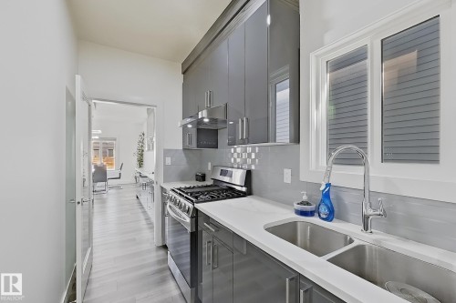 Modern kitchen featuring grey cabinetry, stainless steel appliances, a double basin sink, white countertops, and wood-finish flooring - 415 42 Street, Edmonton, AB 