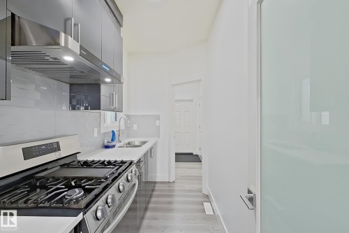 Modern kitchen featuring stainless steel appliances, a gas range with an overhead vent hood, white countertops, and gray wood-finish flooring - 415 42 Street, Edmonton, AB 