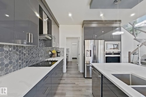 Contemporary kitchen featuring sleek gray cabinetry, light countertops, integrated stainless steel appliances, a hexagonal tile backsplash, and wood-finish flooring - 415 42 Street, Edmonton, AB 
