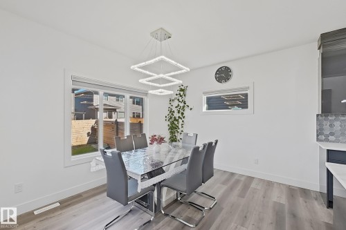 Spacious dining area featuring wood-finish flooring, a contemporary multi-tier chandelier, and large windows providing ample natural light - 415 42 Street, Edmonton, AB 