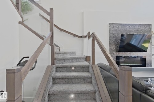 Staircase featuring light gray carpeted treads, integrated step lighting, and a glass panel railing system with wood-finish newel posts and handrails - 415 42 Street, Edmonton, AB 
