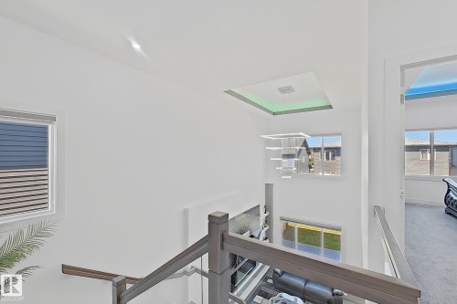 Upper-level landing featuring a wood-finish handrail with glass paneling, an overhead recessed light fixture, and white walls - 415 42 Street, Edmonton, AB 