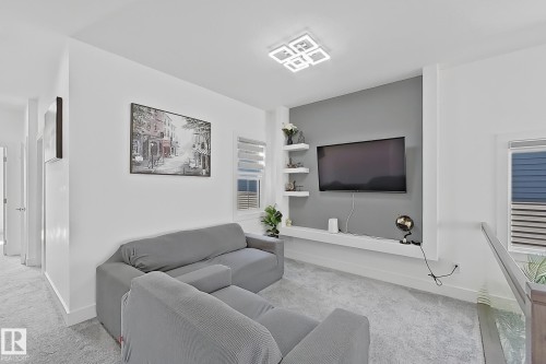 Carpeted landing area featuring a modern flush-mount ceiling light fixture, a media wall with a contrasting accent panel, built-in shelving, and a built-in media console - 415 42 Street, Edmonton, AB 